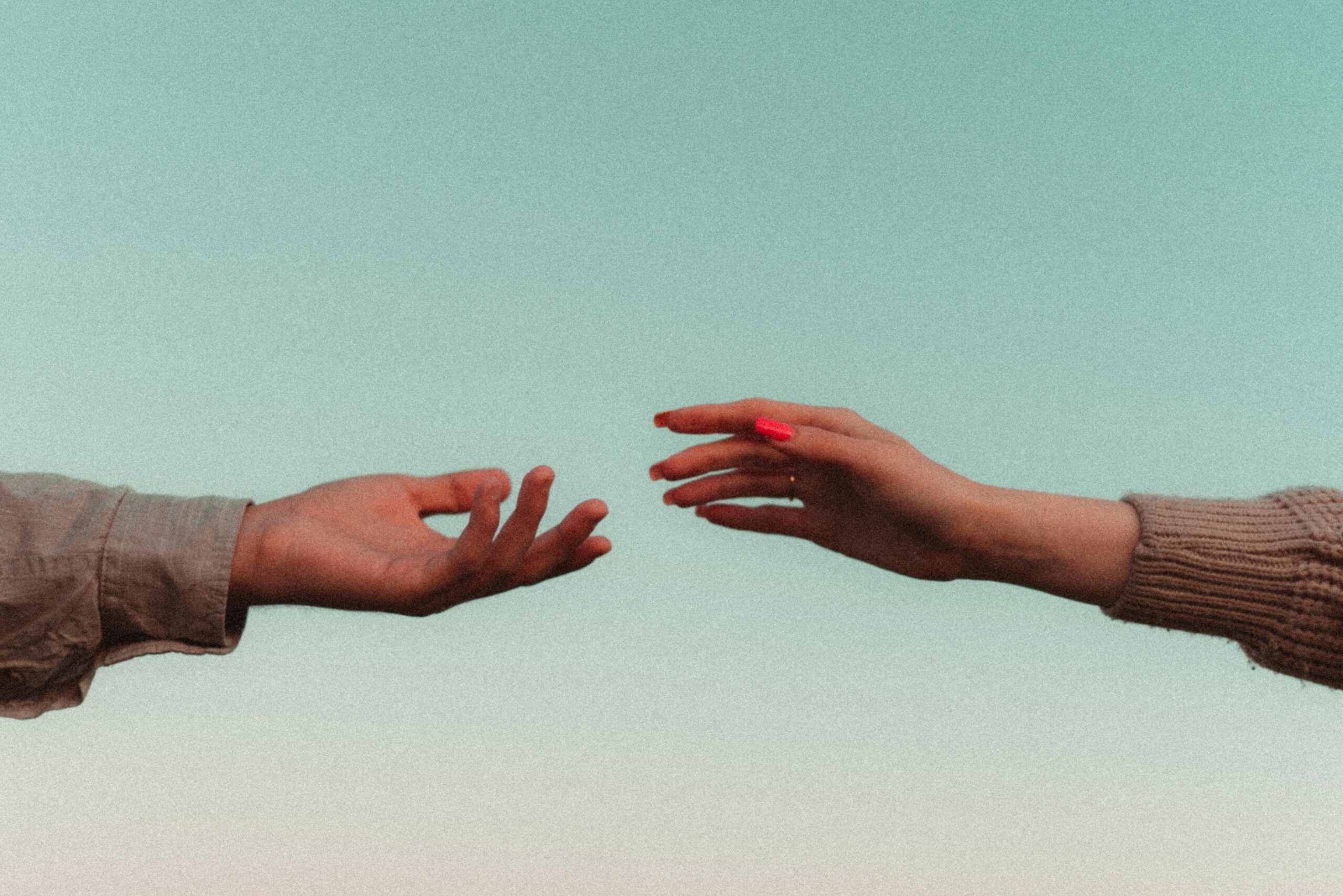 Two hands reaching towards each other with a sky backdrop, symbolizing connection and unity.